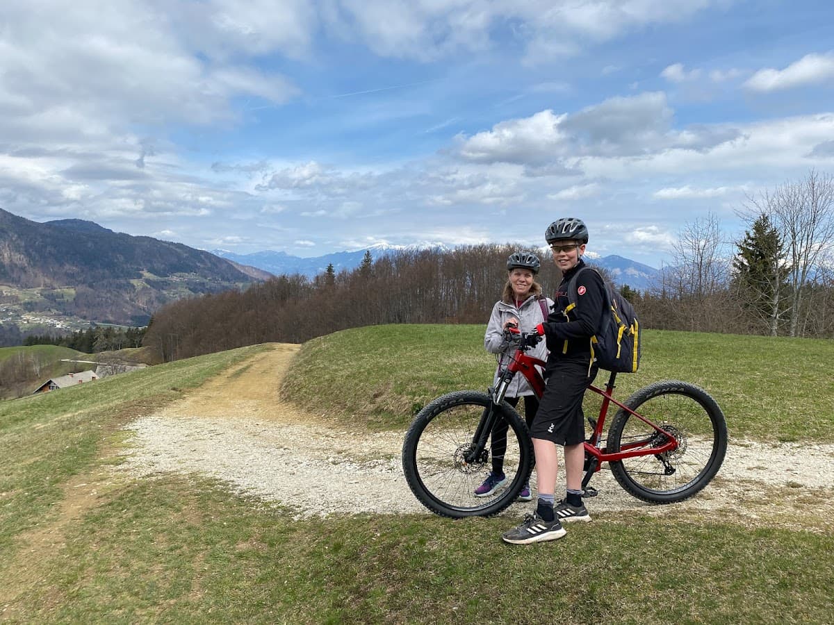 Mountain biking with two people and a red bike on a grassy trail overlooking forested hills.
