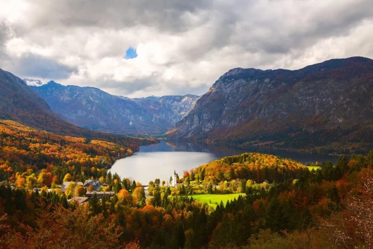 Lake Bohinj in Triglav National Park with autumn foliage and dramatic cloudy sky.