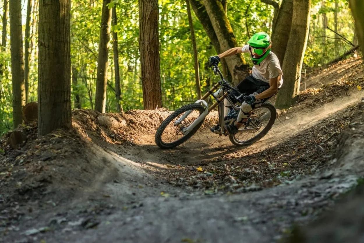 Mountain biker takes a berm on a dirt trail in a sunny forest setting, Golovec bike trail.