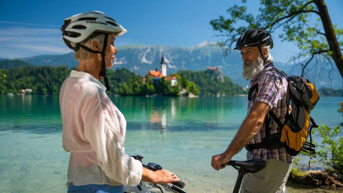 Cyclists with bikes by Lake Bled, Slovenia, with island church and mountains.