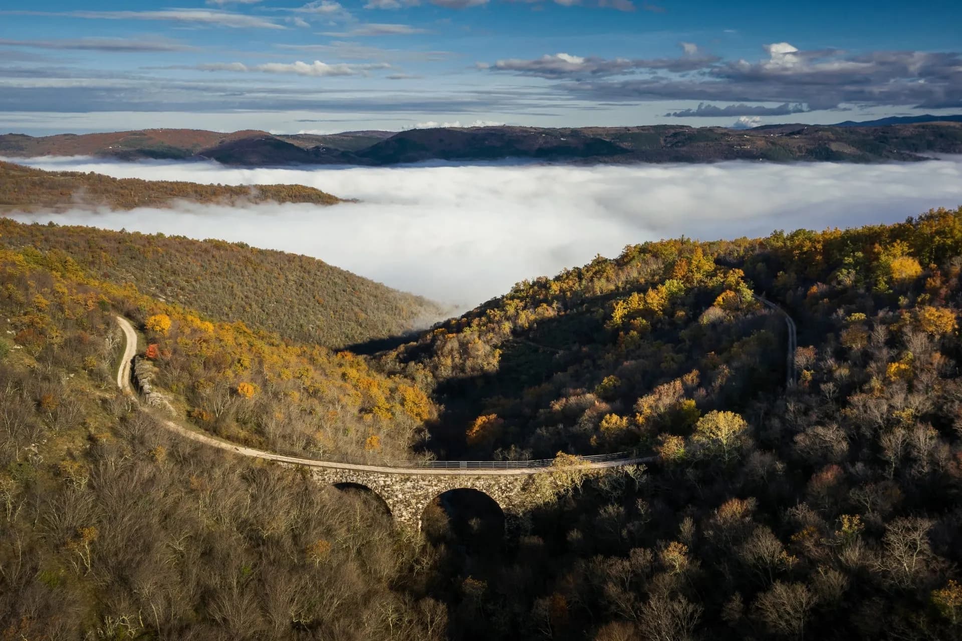 Former Parenzana railroad stone viaduct over valley filled with low clouds and autumn foliage.