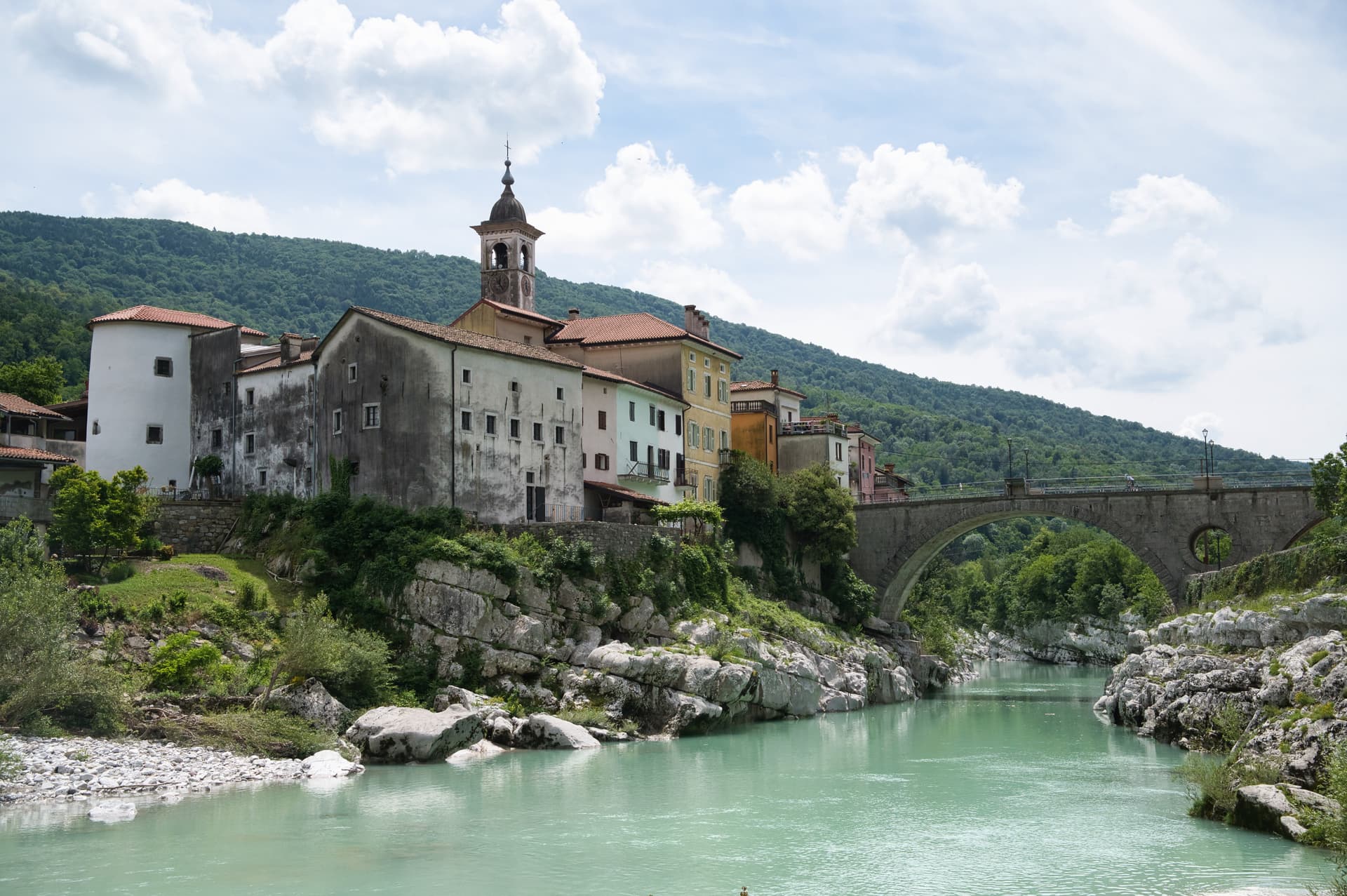 Cyclist on stone bridge over turquoise river near colorful buildings in Soca Valley