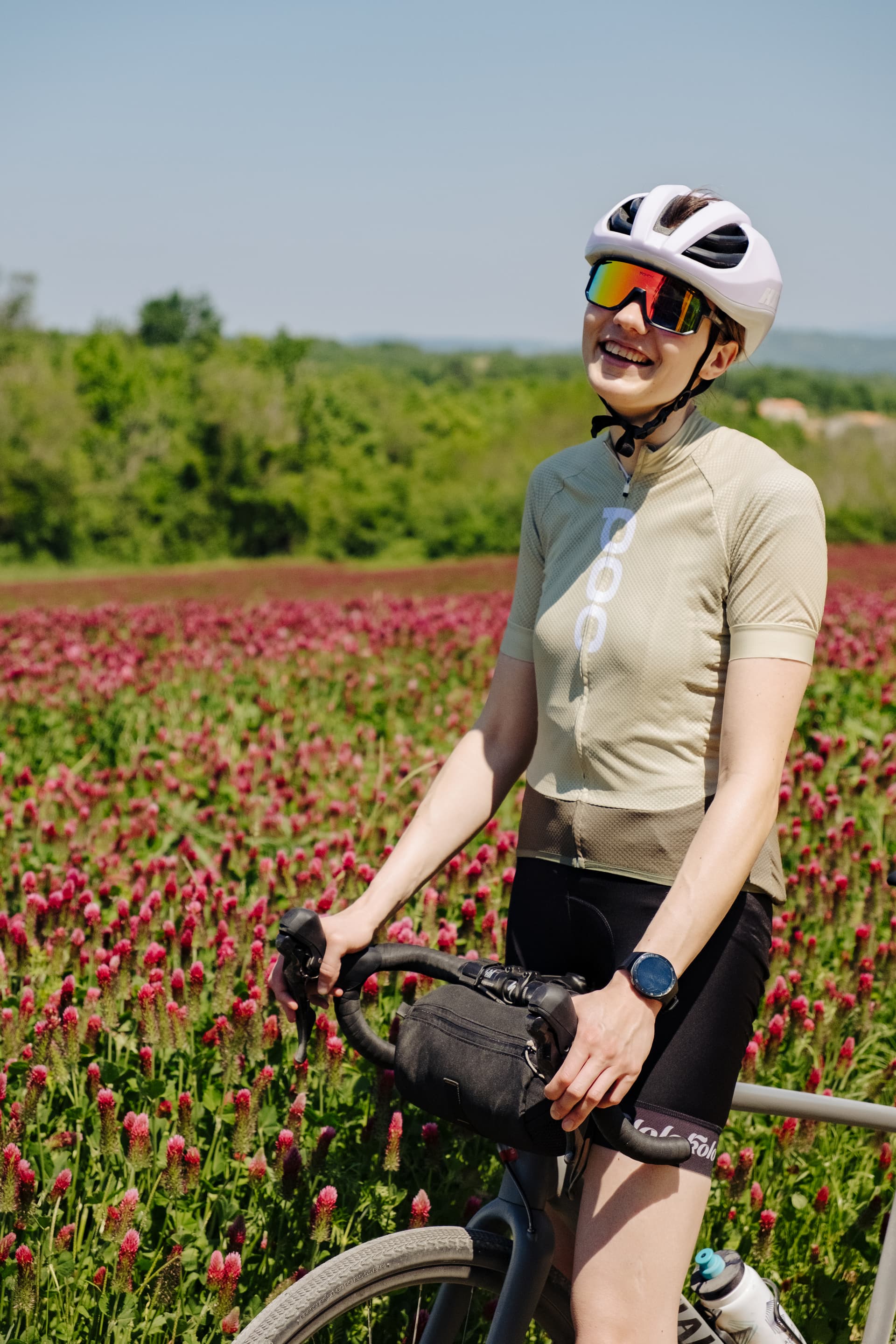 Cyclist taking a break by a field of red clover flowers with green trees in the background.