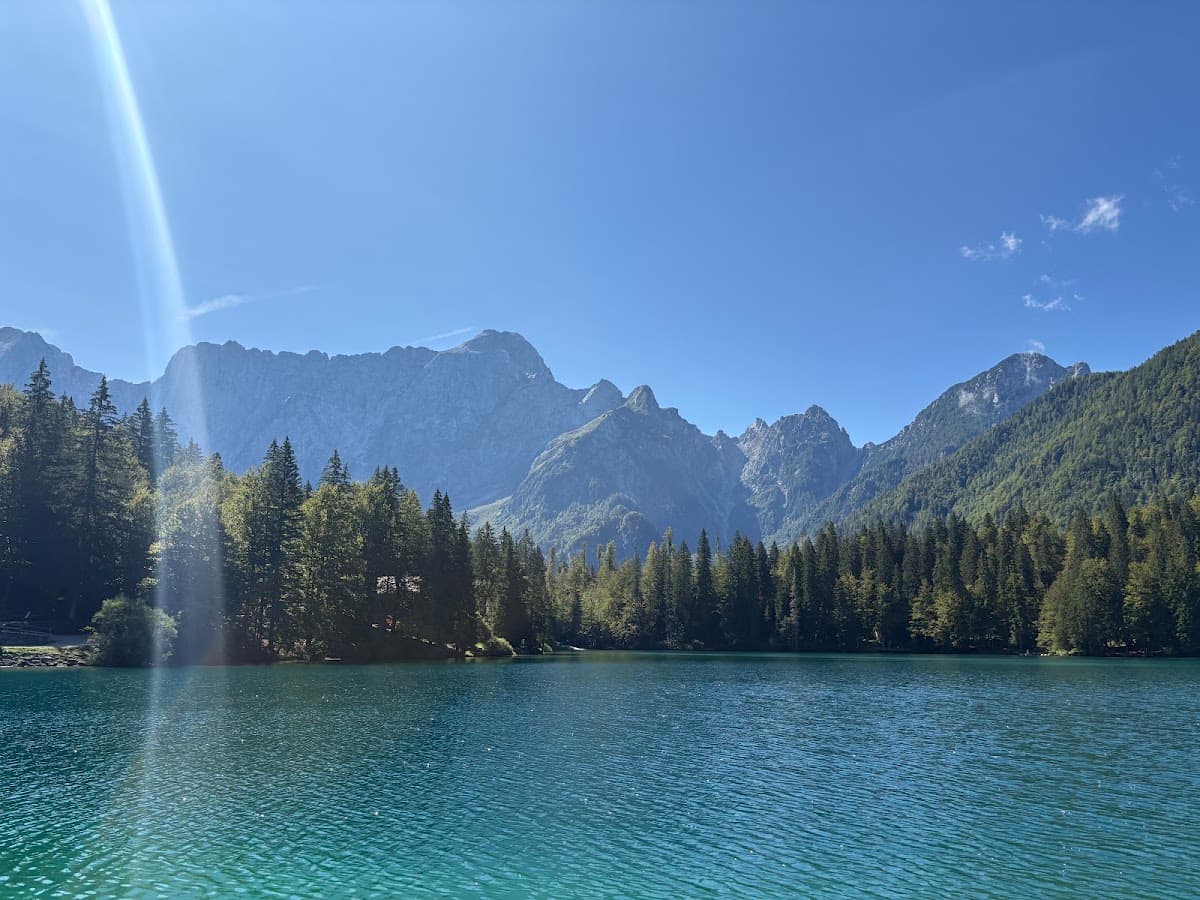 Alpine lake with turquoise water, pine forest, and rocky mountain peaks under blue sky