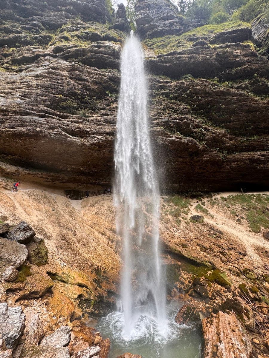Waterfall cascading over rocky cliff face into a pool with a walking path behind it