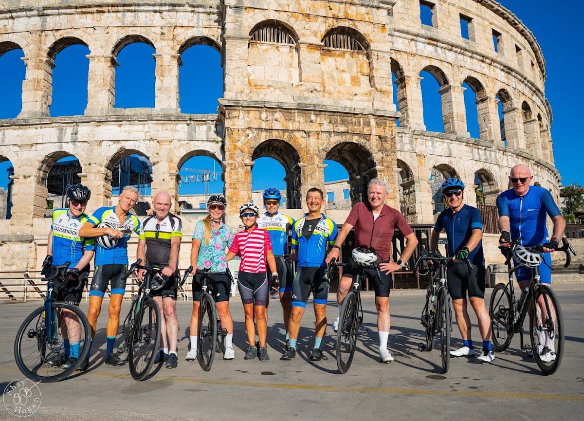 Cyclists posing with bicycles in front of a Roman amphitheater