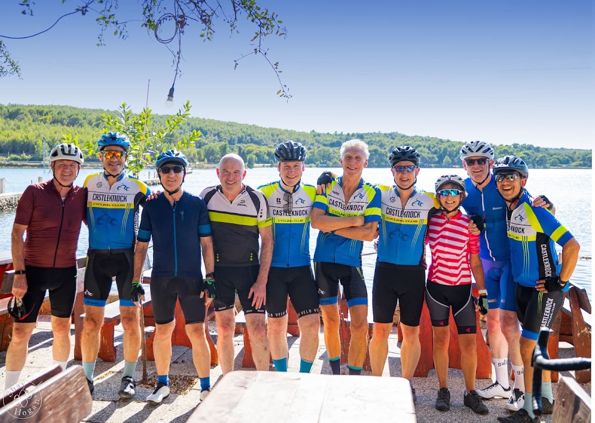 Group of cyclists in matching jerseys standing together by a lake