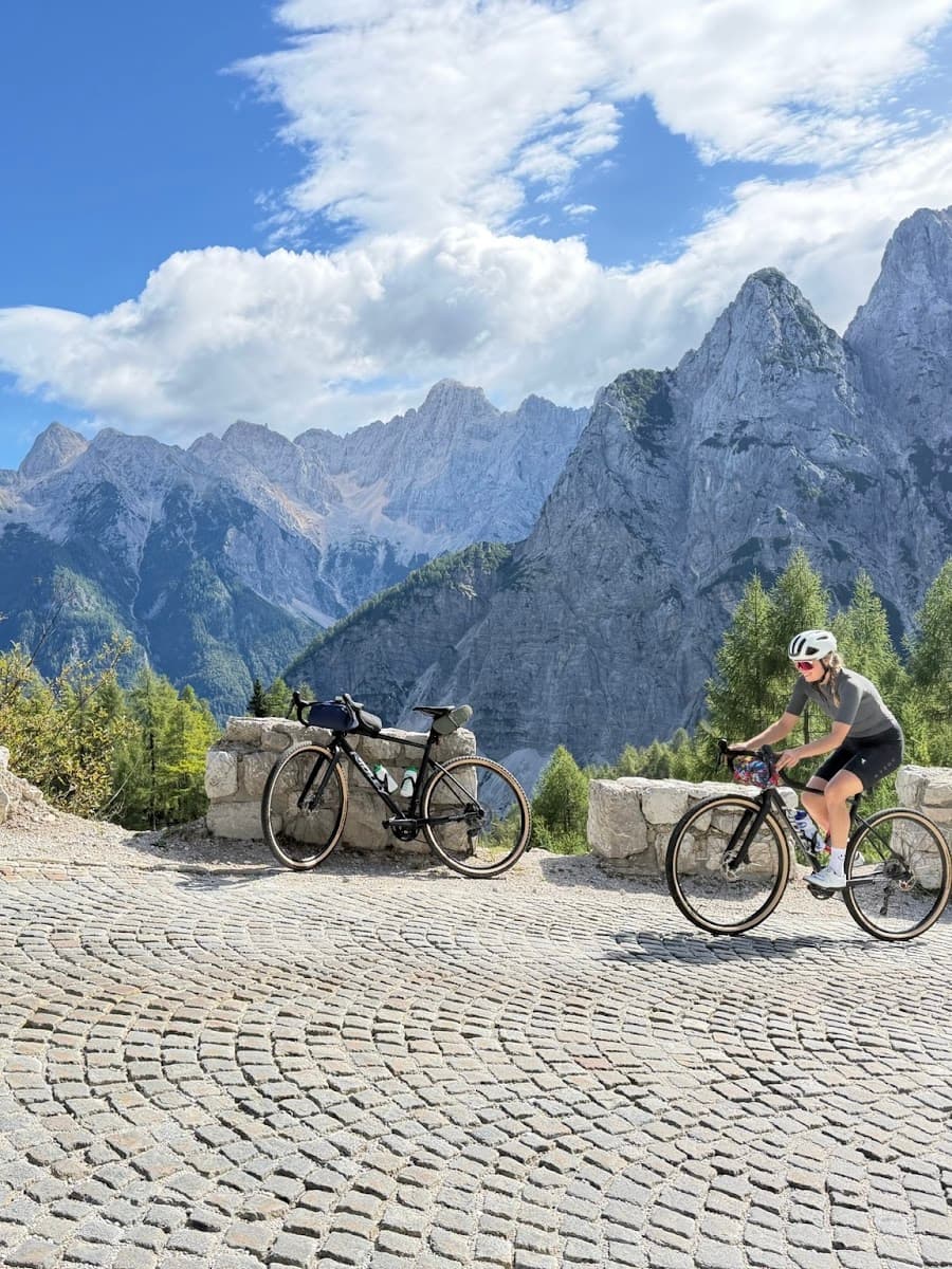 Cyclists on a cobblestone mountain road with dramatic alpine peaks in the background