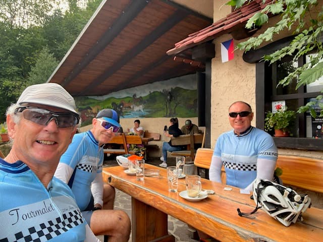 Cyclists sitting at an outdoor wooden table at a cafe patio