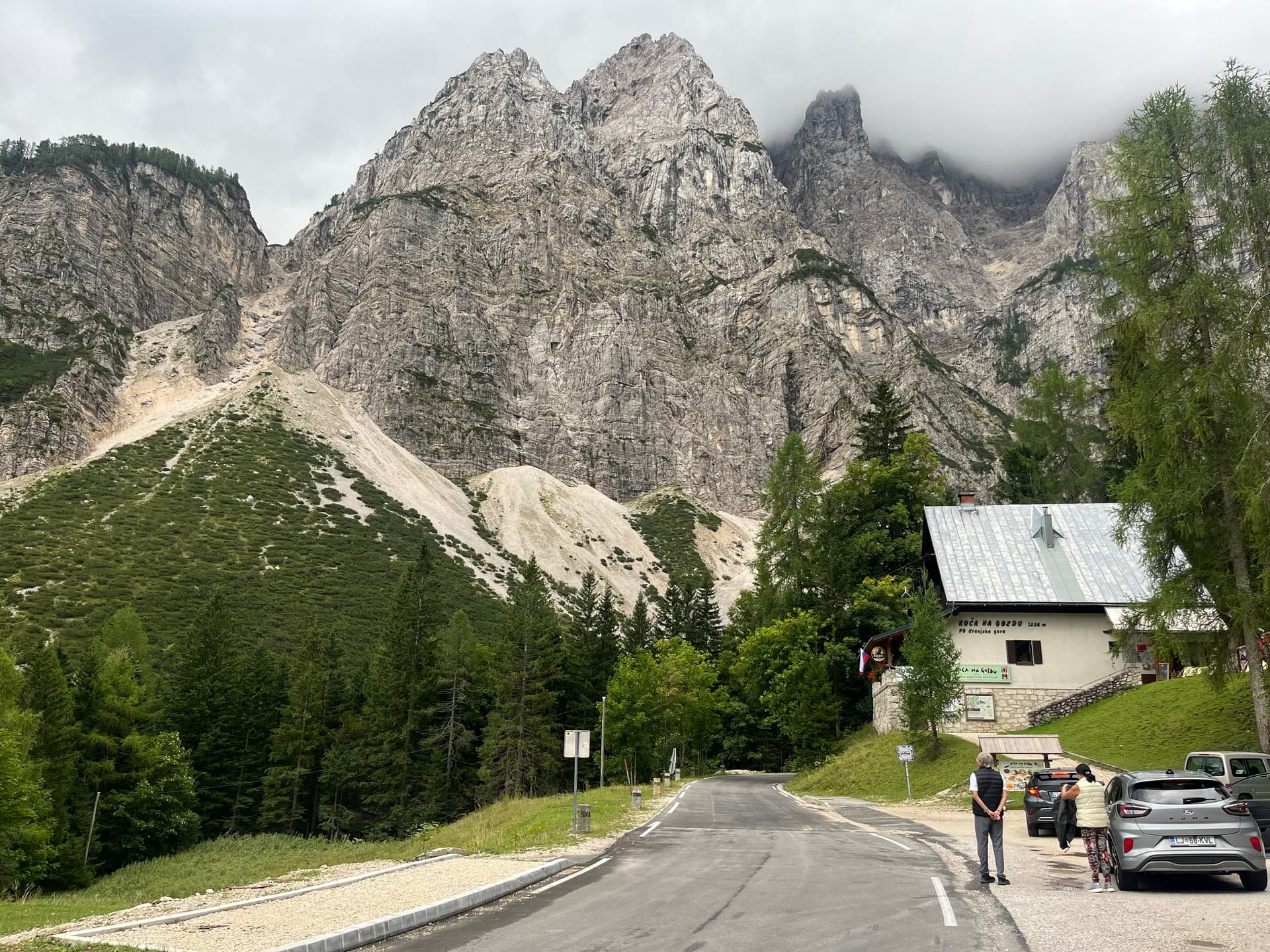 Road below huge limestone peaks with parked cars and building