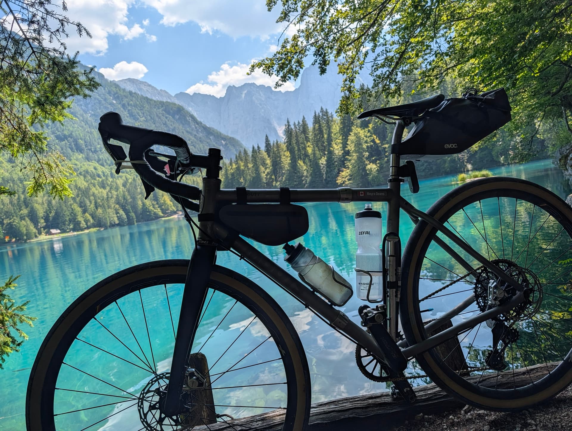 Gravel bike parked by a turquoise alpine lake with mountains and forest