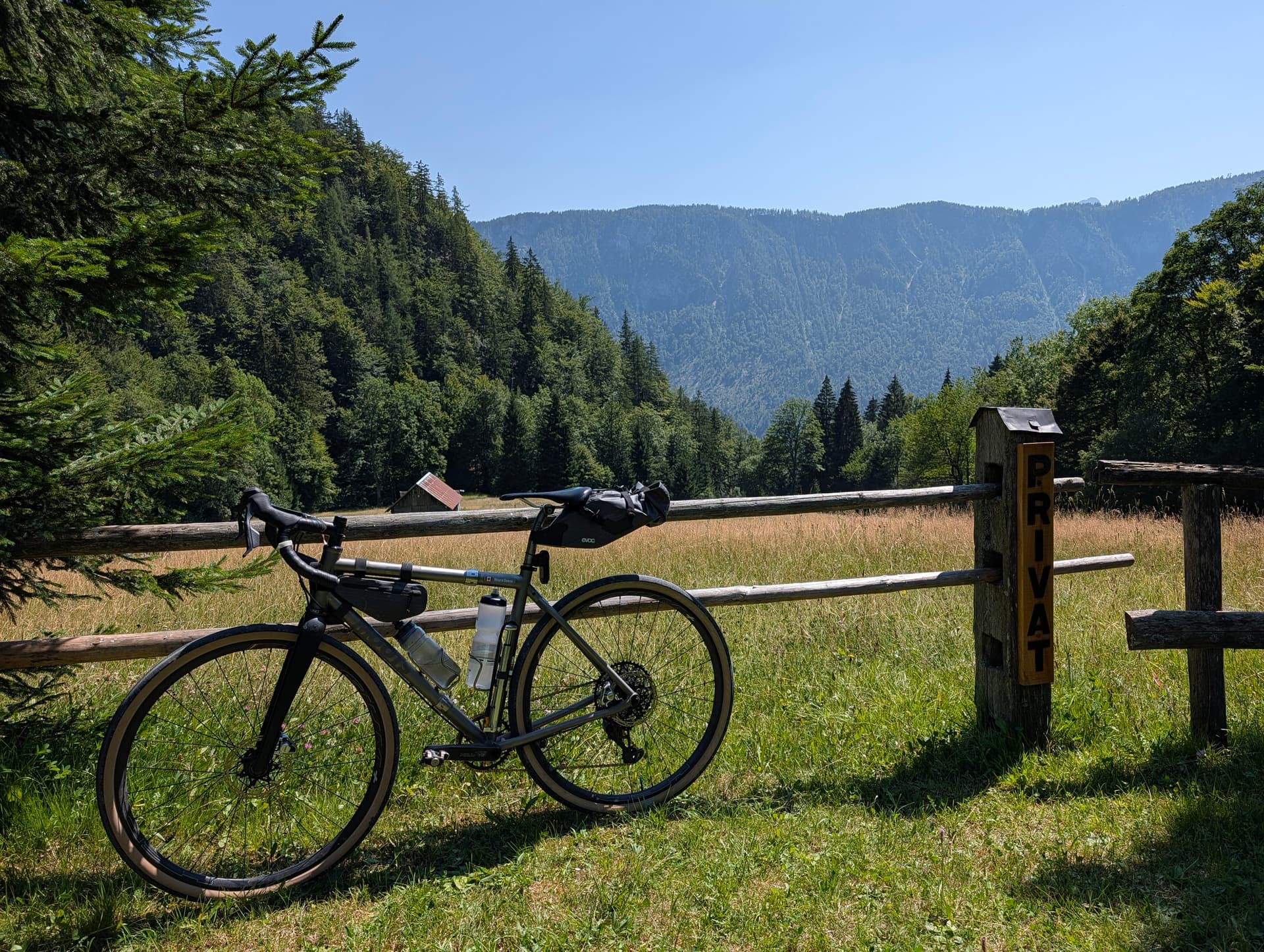 Gravel bike parked by wooden fence in mountain meadow with forest and peaks