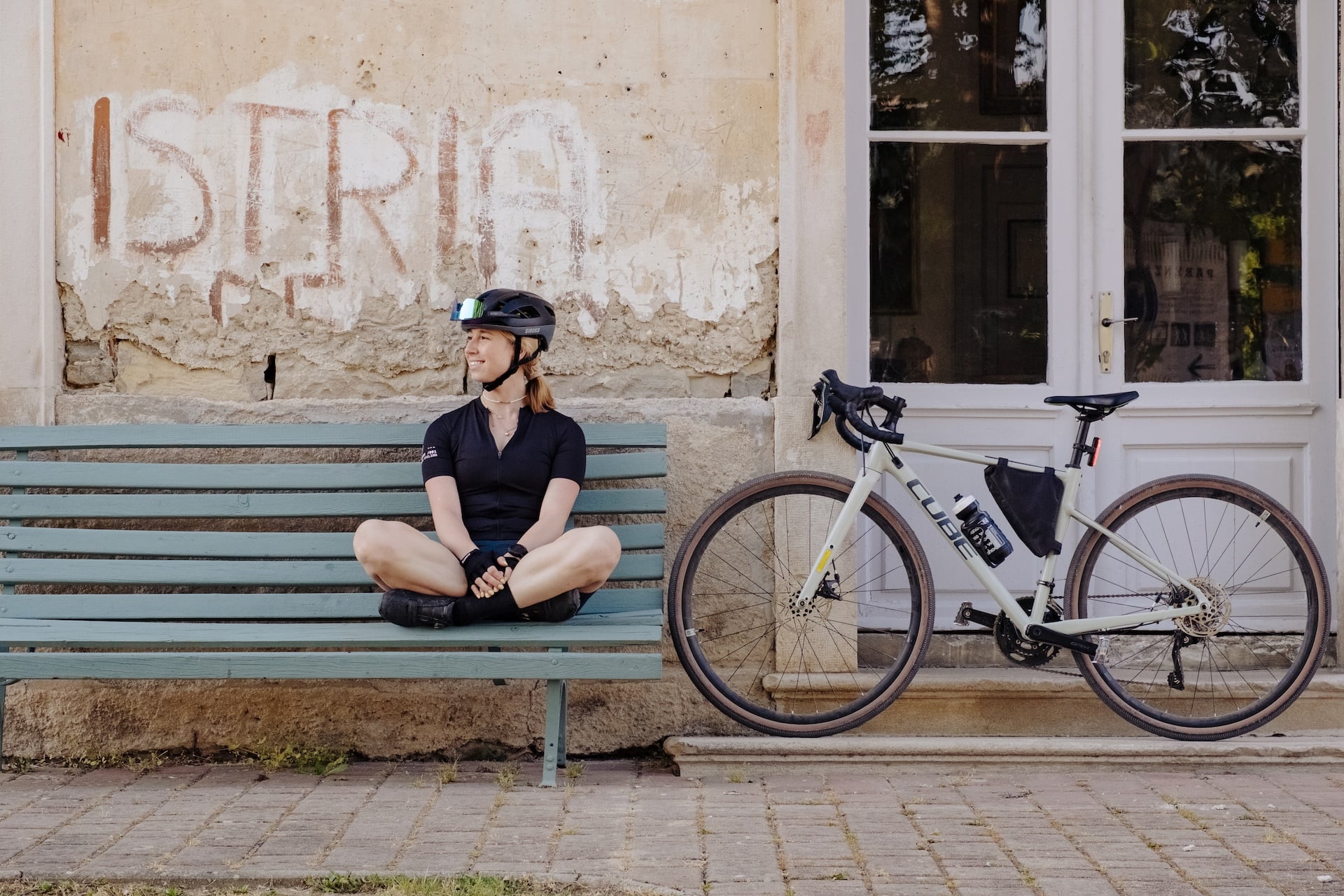 Cyclist resting on bench next to gravel bike, "Istria" painted on weathered wall.