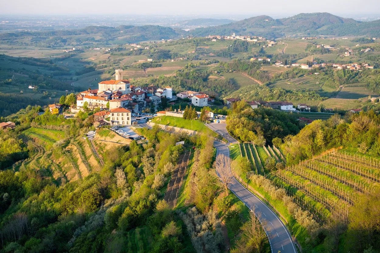 Hilltop village in Goriška Brda with vineyards and winding road in rolling green hills.