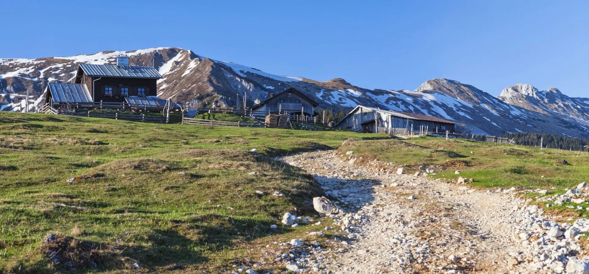 Mountain pasture with wooden huts and snow-dusted peaks at Kofce.