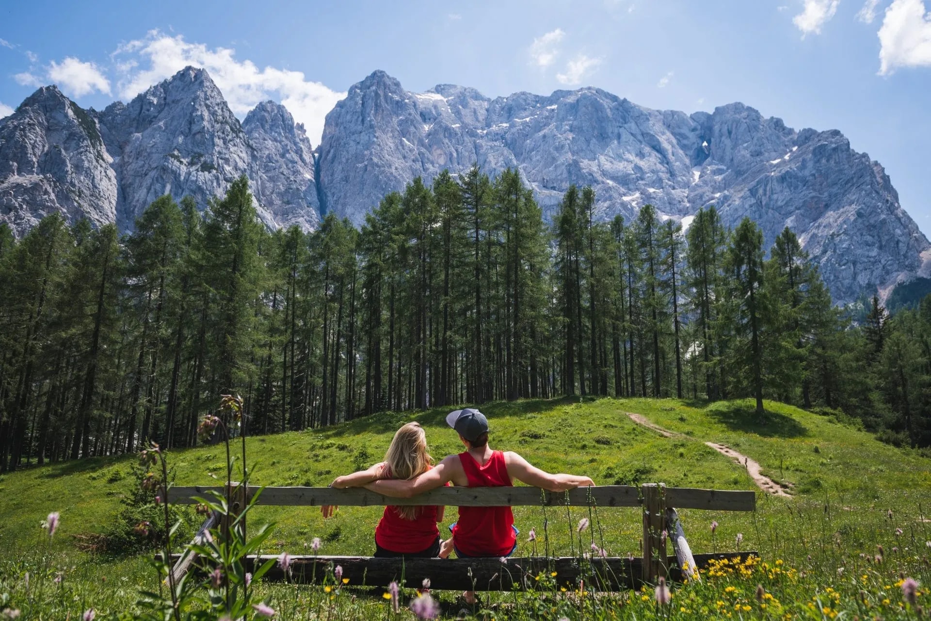 Couple relaxing on bench overlooking Vršič Pass mountains and pine forest