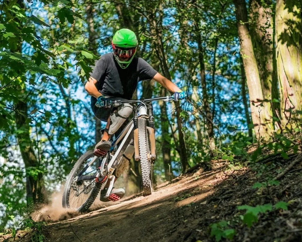 Mountain biker in green helmet descending dirt trail through sunny forest in Slovenia