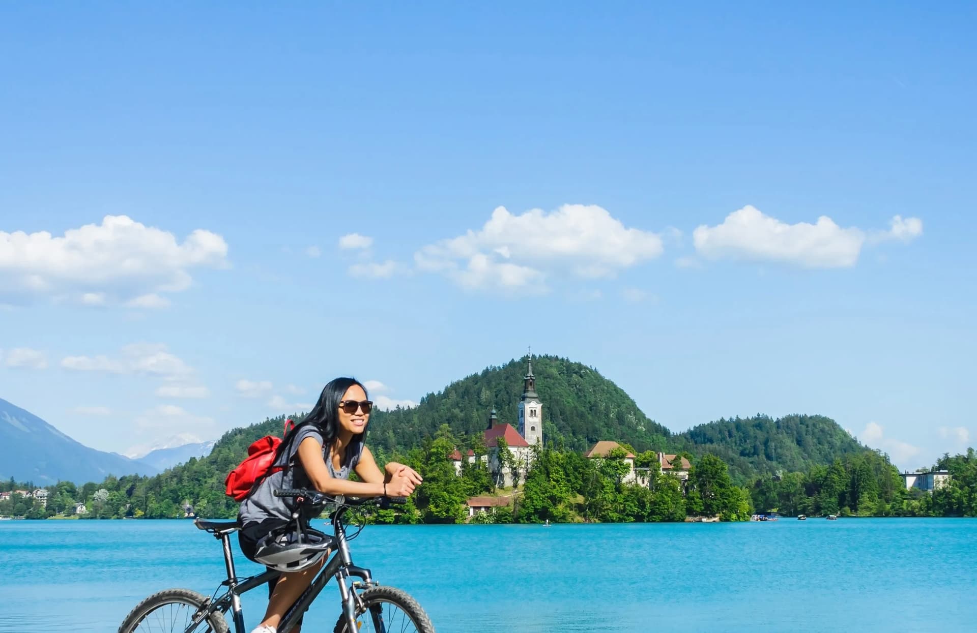 Cyclist with red backpack by turquoise Lake Bled with island church and mountains