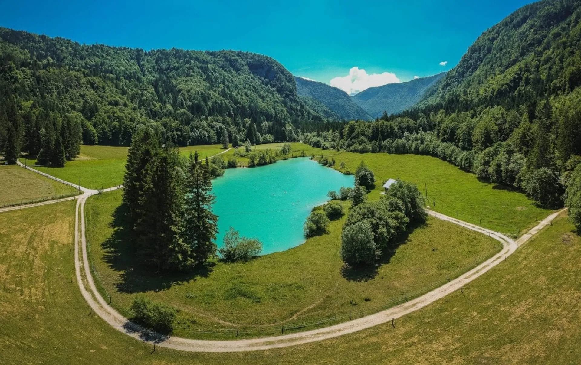 Turquoise Kreda lake surrounded by green meadows and forested mountains in Radovna Valley.