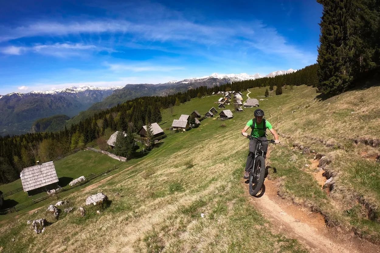 Mountain biking near Zajamniki alpine village with snow-capped Julian Alps in background
