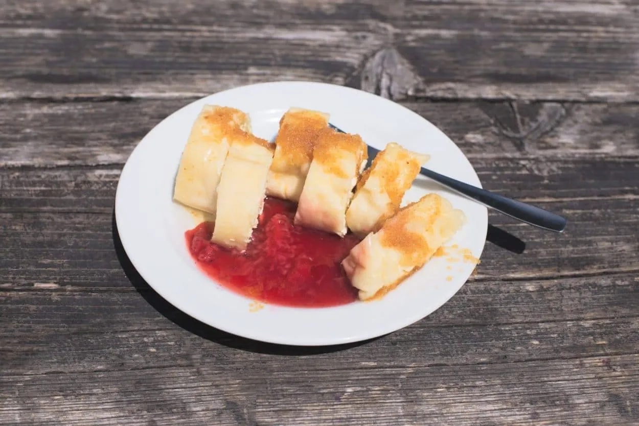 Struklji dessert with strawberry sauce on a white plate on a rustic wooden table.