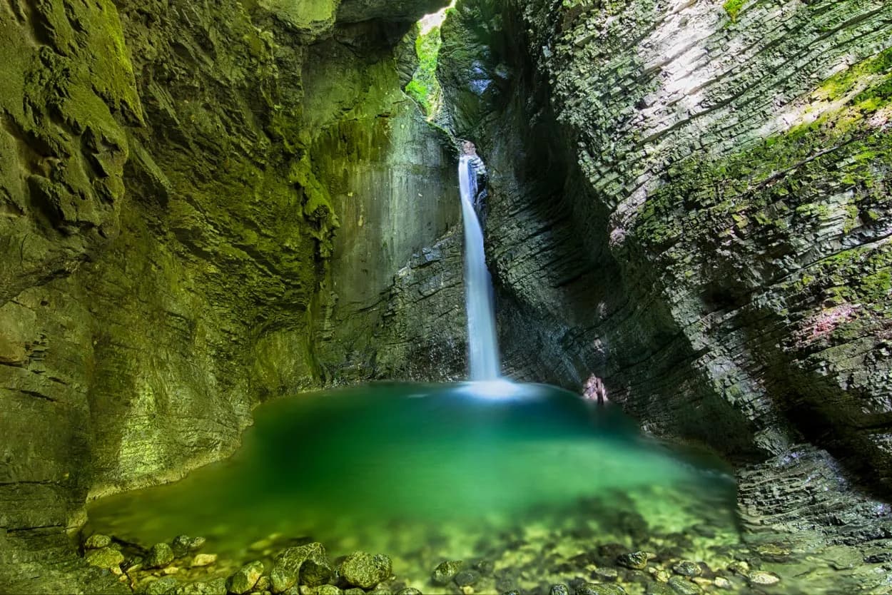 Waterfall plunging into a green pool inside a moss-covered rock gorge, Kozjak Waterfall.