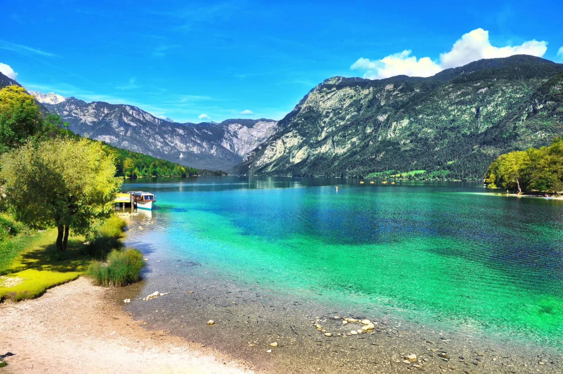 Bohinj Lake with turquoise water, mountains of Triglav National Park, and a boat docked near shore.