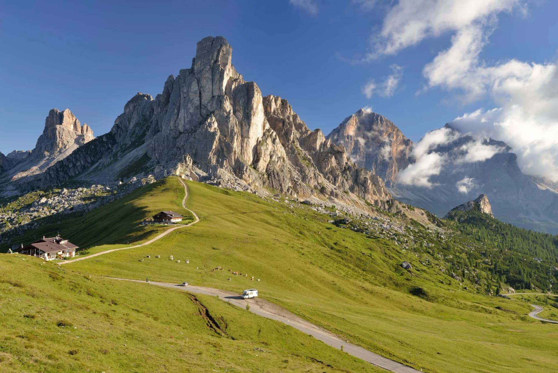 Passo Giau view with jagged limestone peaks, green alpine meadow, and winding road.
