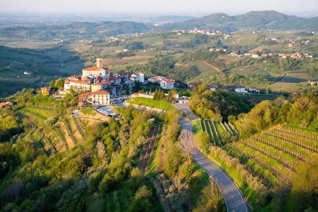 Hilltop village of Goriška Brda surrounded by green, terraced vineyards and rolling hills.
