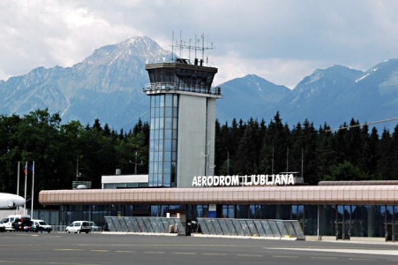 Aerodrom Ljubljana control tower with mountains and forest backdrop.
