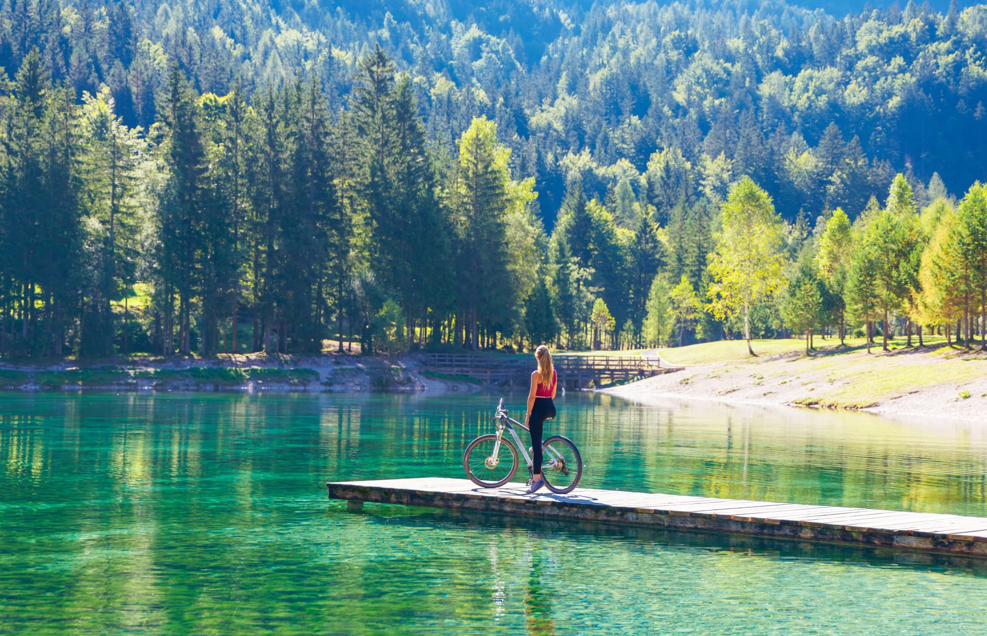 Woman on bike on wooden pier enjoying breathtaking landscape, green lake in the mountain- Slovenia- travel, sport, wanderlust concept
