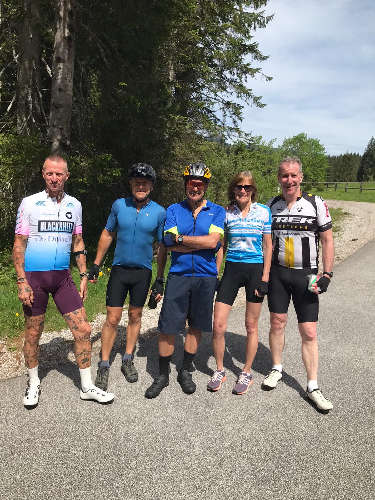 Cyclists posing on paved road near forest on Pokljuka Plateau.