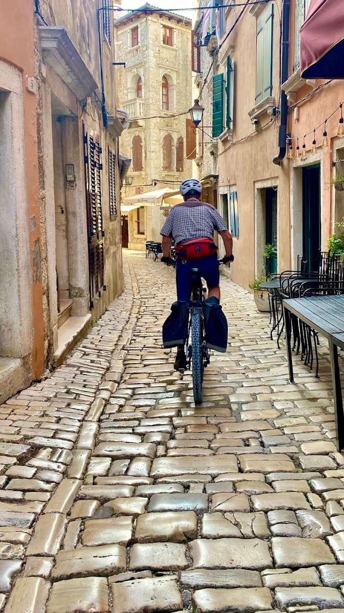 Cyclist with panniers riding up a narrow cobblestone street in a historic town.