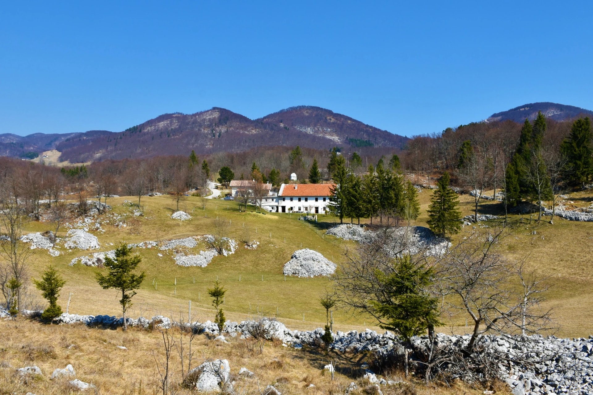 Contryside at the Trnovo forest plateau above Ajdovscina in Slovenia with a farm house and forest covered hills above