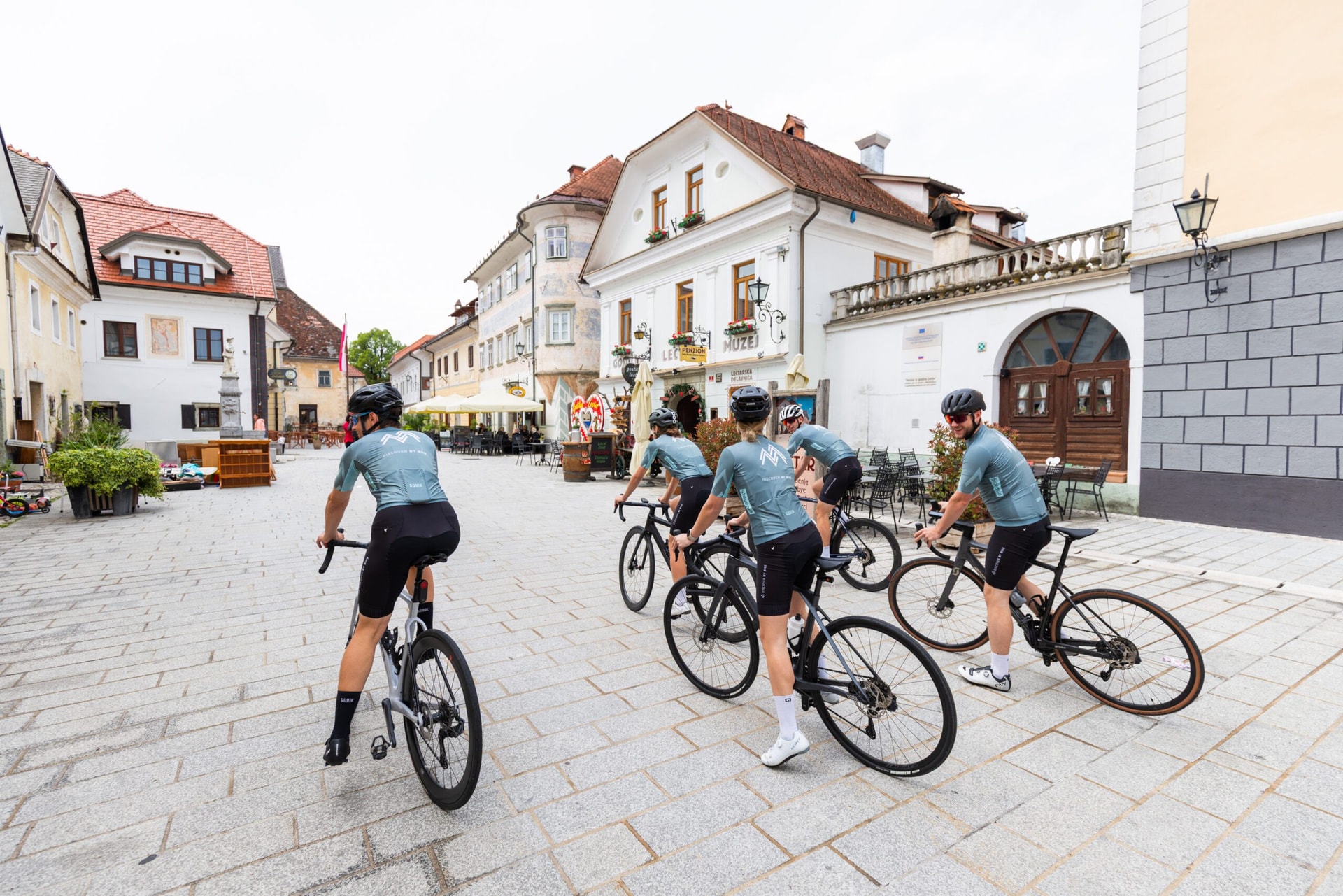 Cyclists riding through a historic European town square with traditional buildings.
