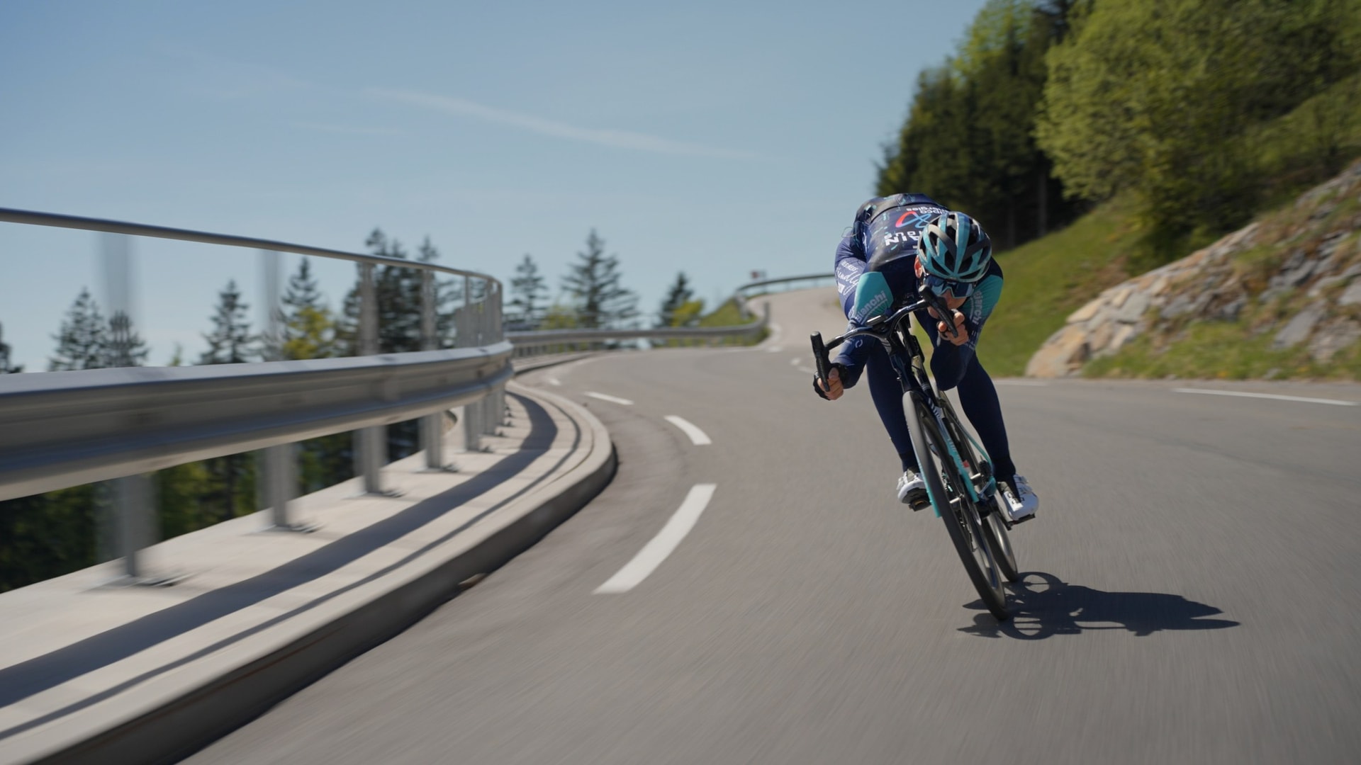 Cyclist descending a mountain hairpin turn on a paved road.