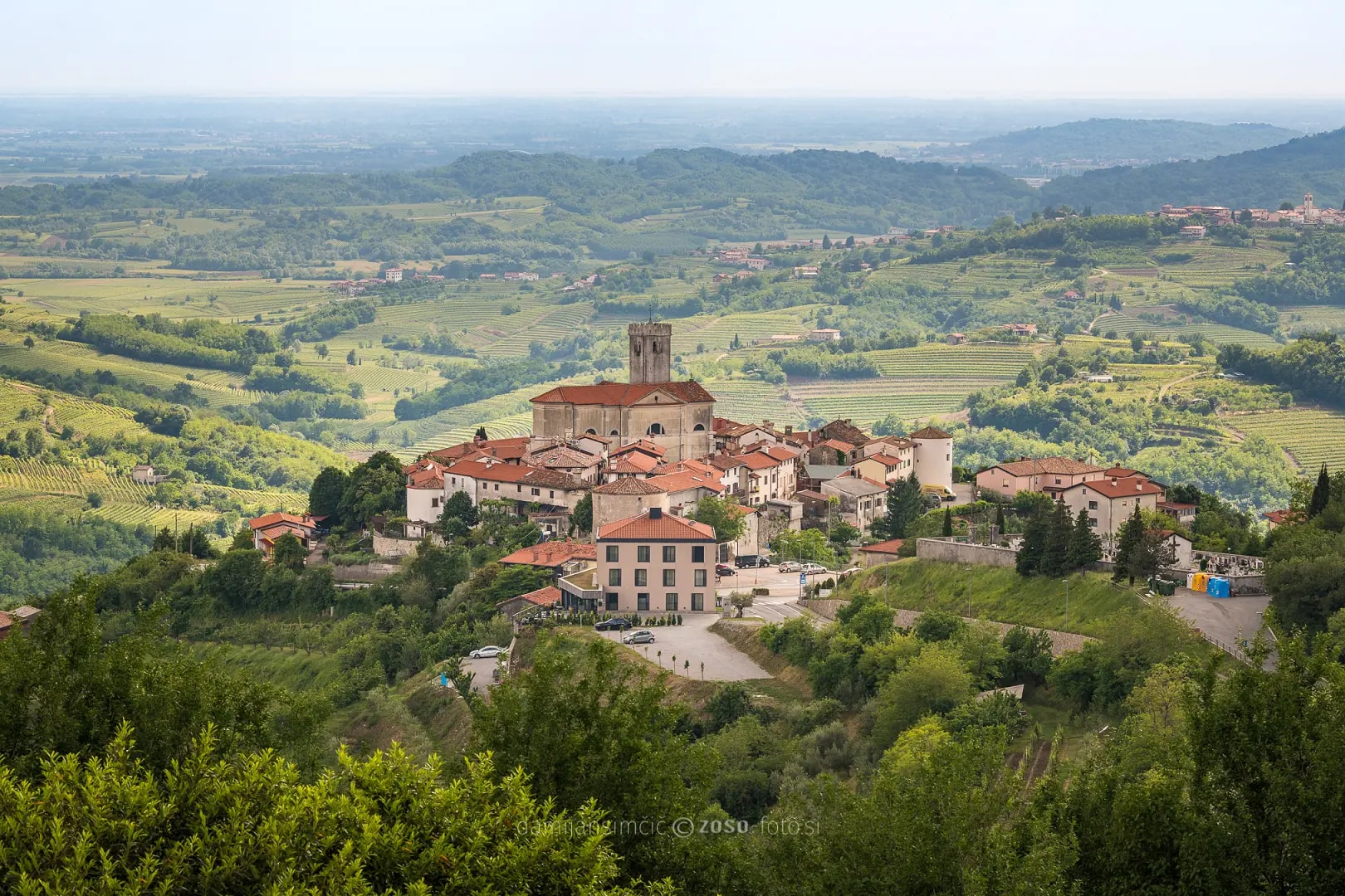 Šmartno village with historic church and terracotta roofs surrounded by vineyards in Goriška Brda, Slovenia.