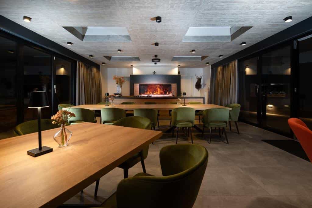 Modern resort dining room with wooden tables, green velvet chairs, and a lit fireplace at Lake Bled, Slovenia.