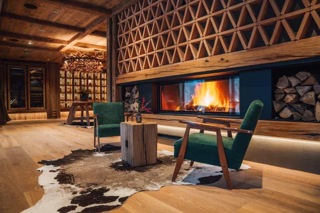 Cozy lounge area with green armchairs, cowhide rug, and fireplace in a rustic wooden interior.