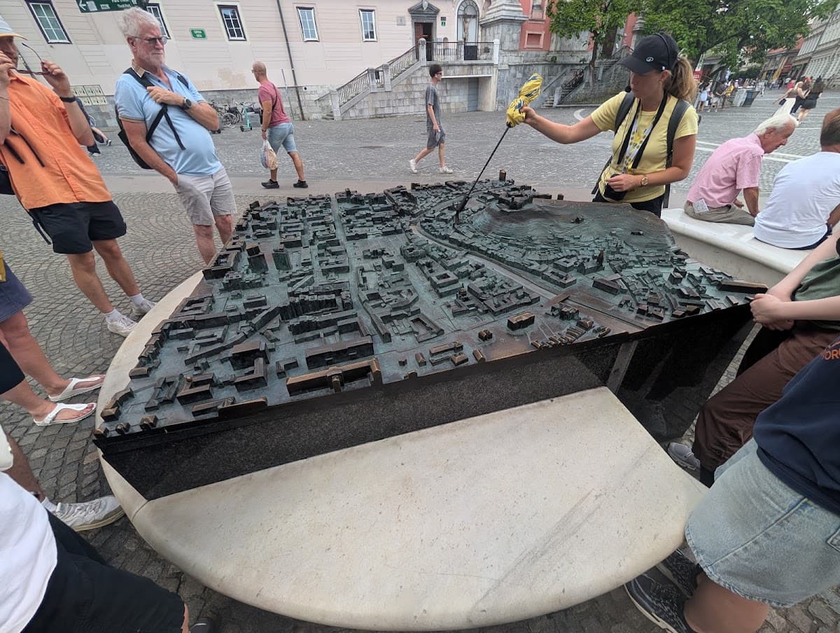 Tour guide pointing at a bronze scale model of a city in a European square