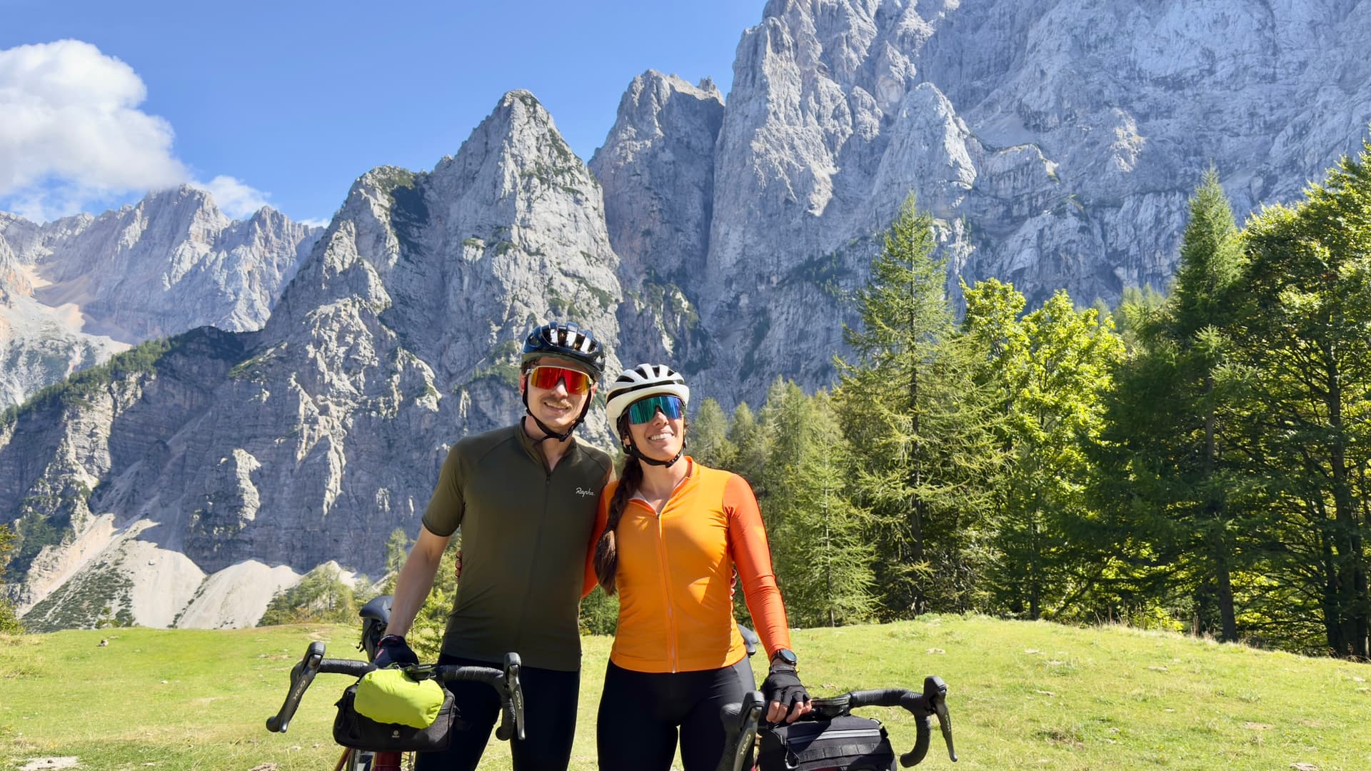 Two cyclists standing with bicycles below Vrsic peaks with jagged mountain backdrop