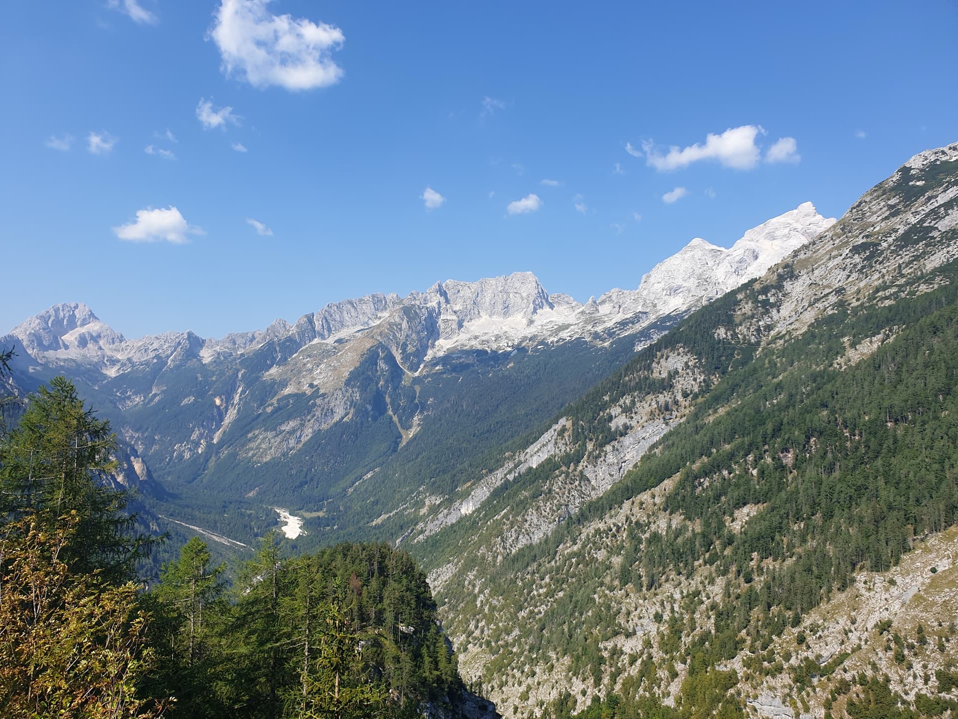 Alpine valley and rocky mountain peaks under a blue sky with scattered clouds