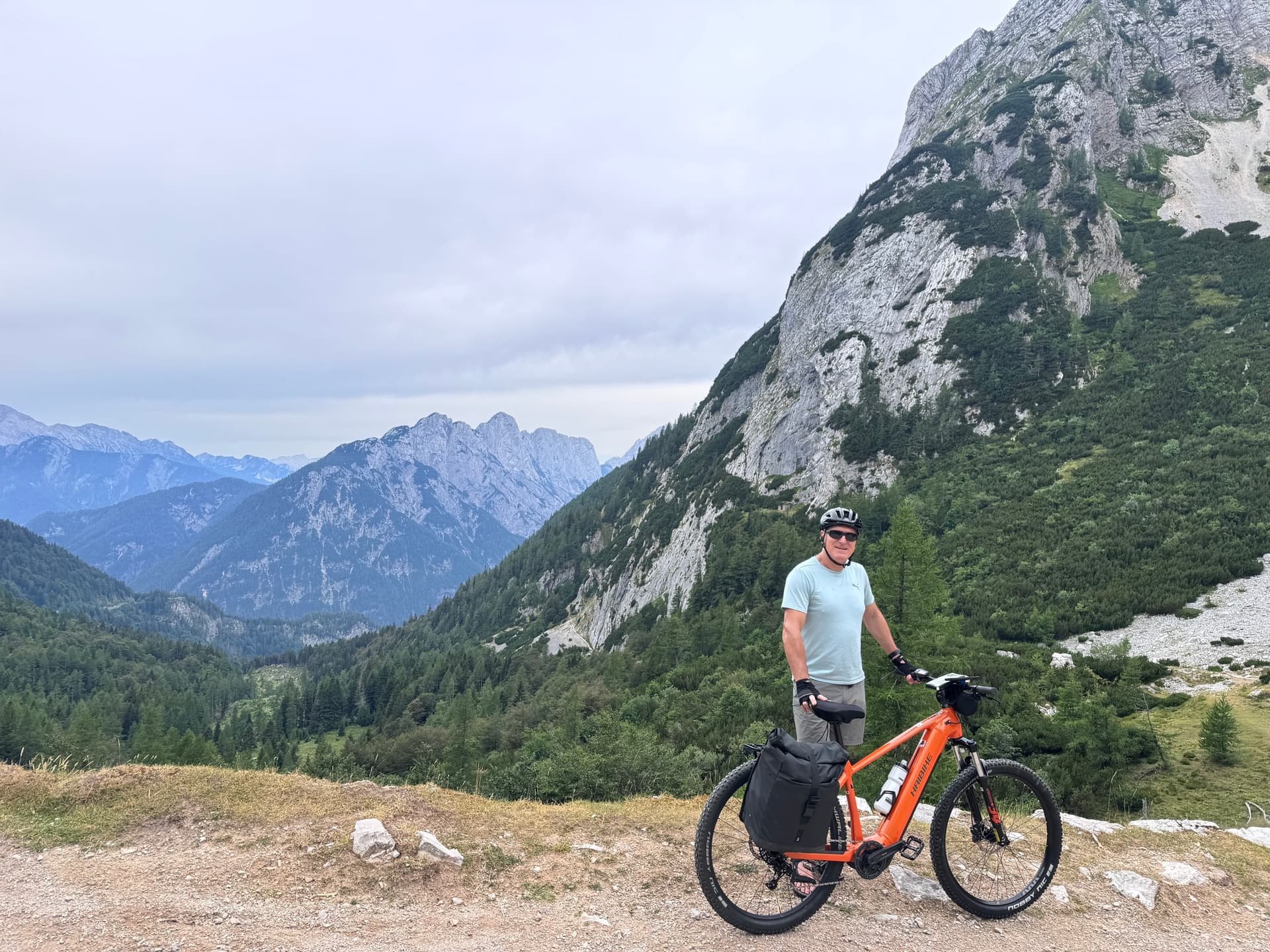 Cyclist with orange e-bike standing on mountain trail above alpine valley