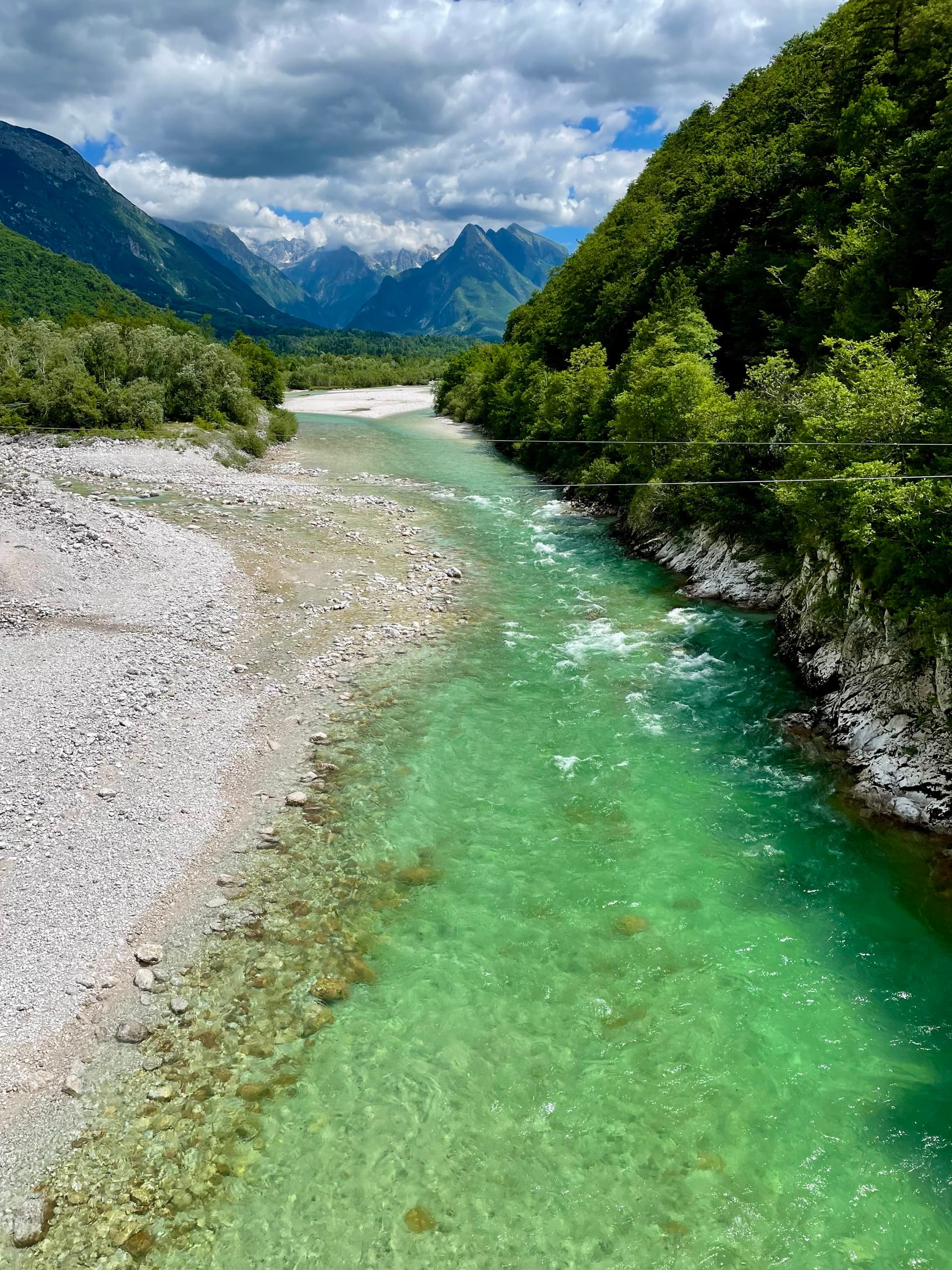 Emerald Soca River flowing between gravel banks and forested mountains under a cloudy sky