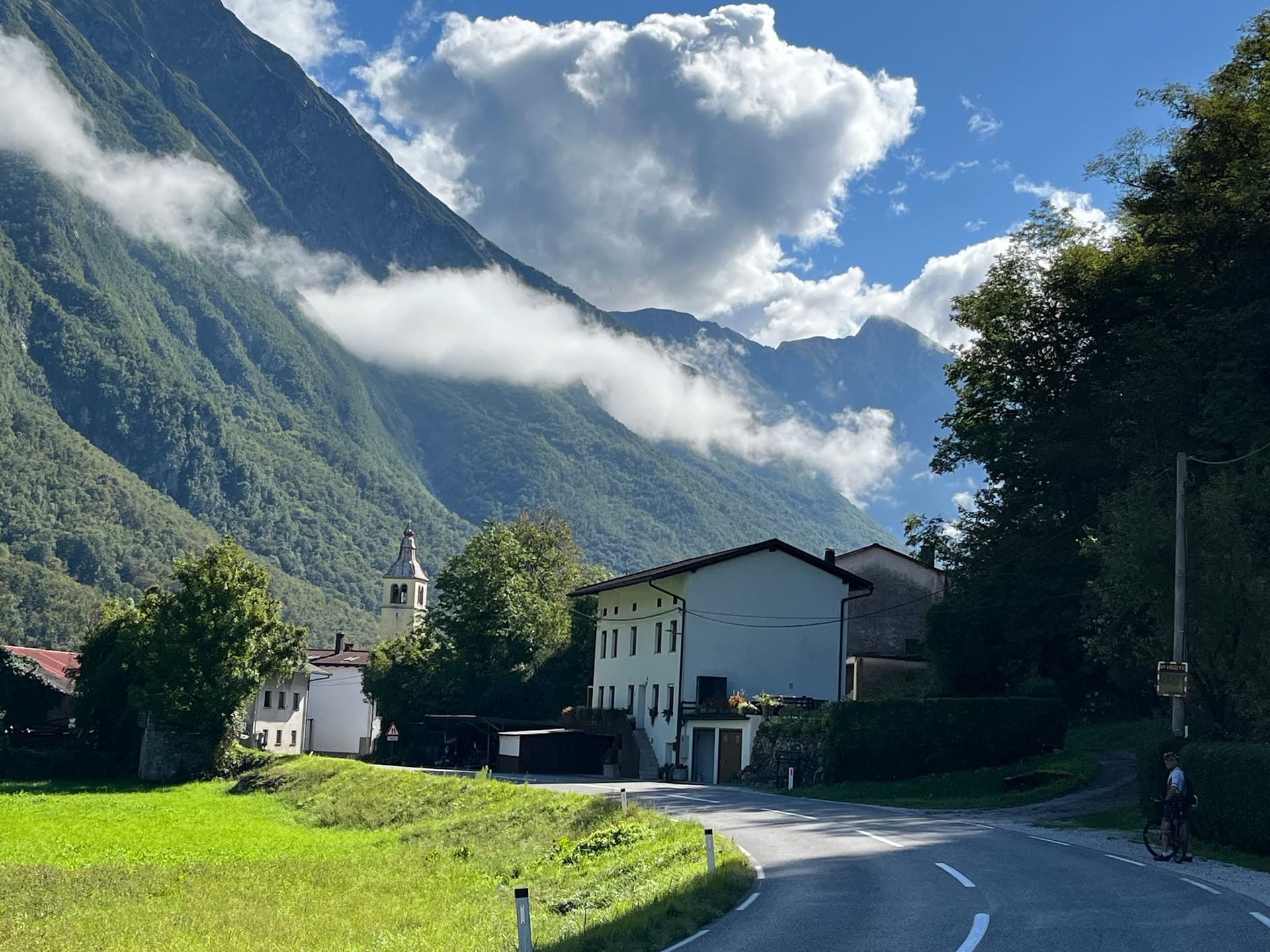 Road curving below steep mountains with clouds and village buildings