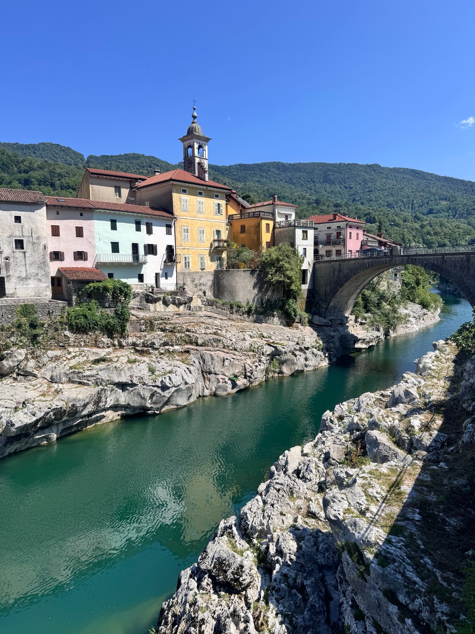 Stone bridge crossing emerald river next to colorful historic buildings in Kanal ob Soči