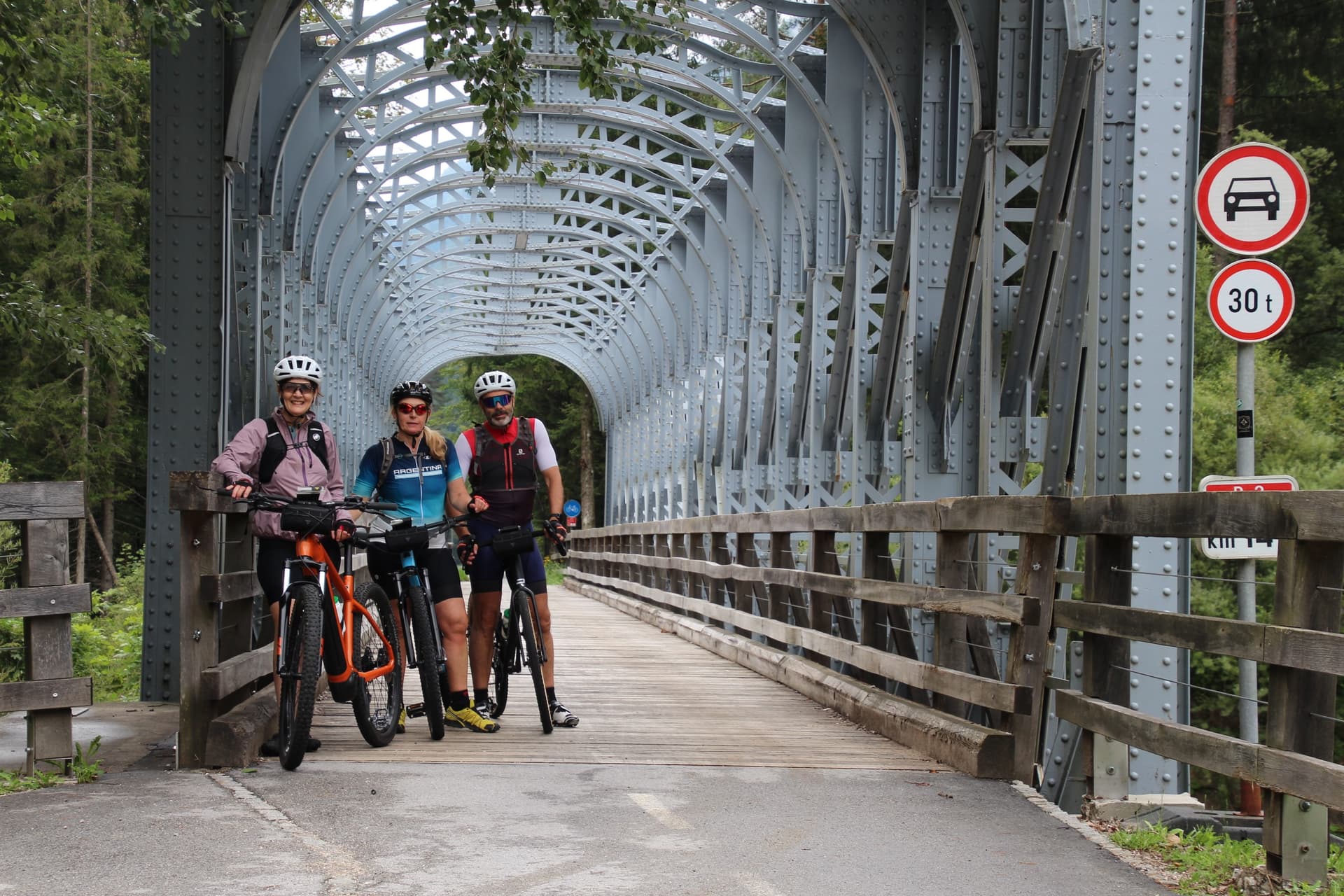 Cyclists with bicycles on a steel truss bridge with wooden deck