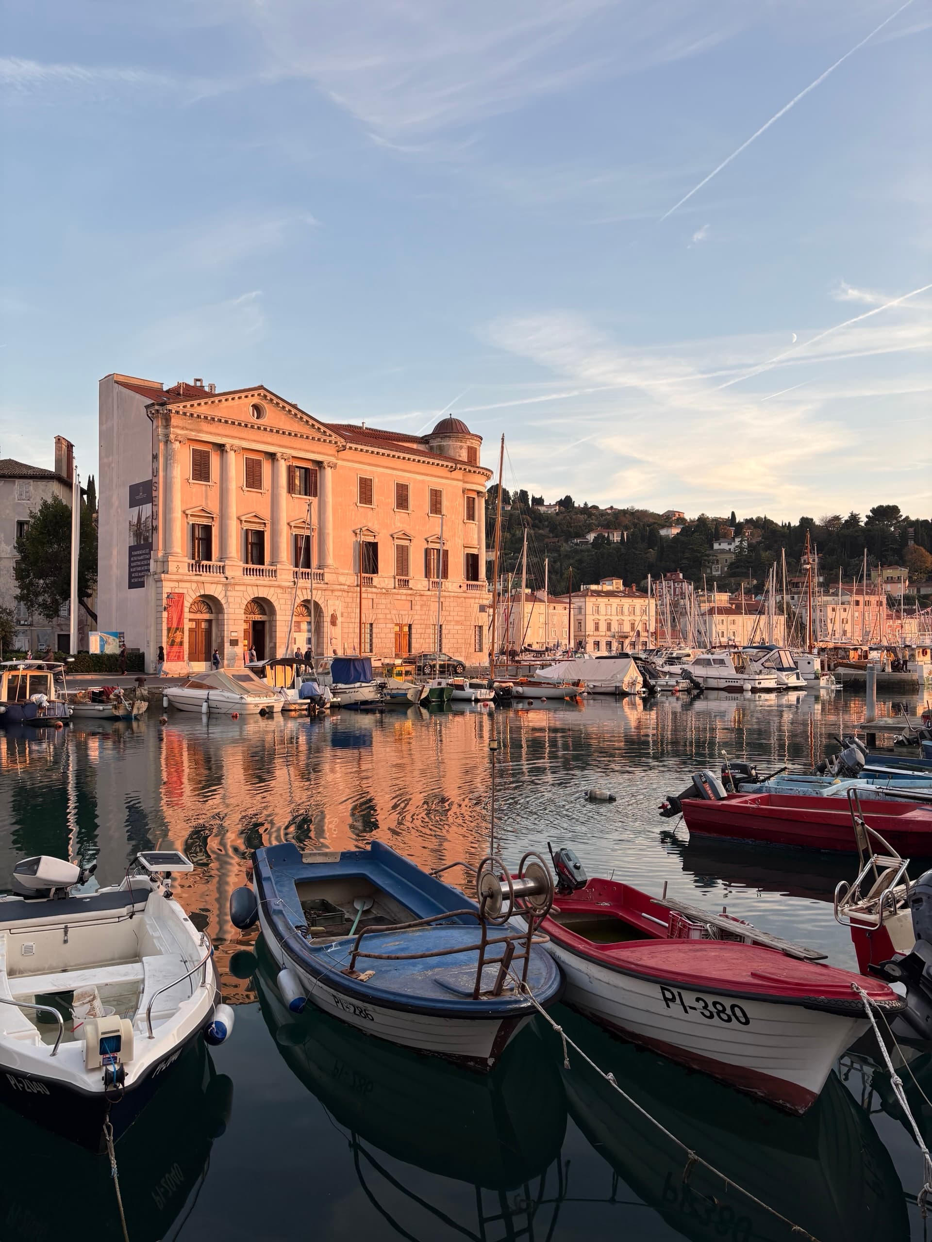 Piran harbor at sunset with docked boats and historic buildings reflected in the water