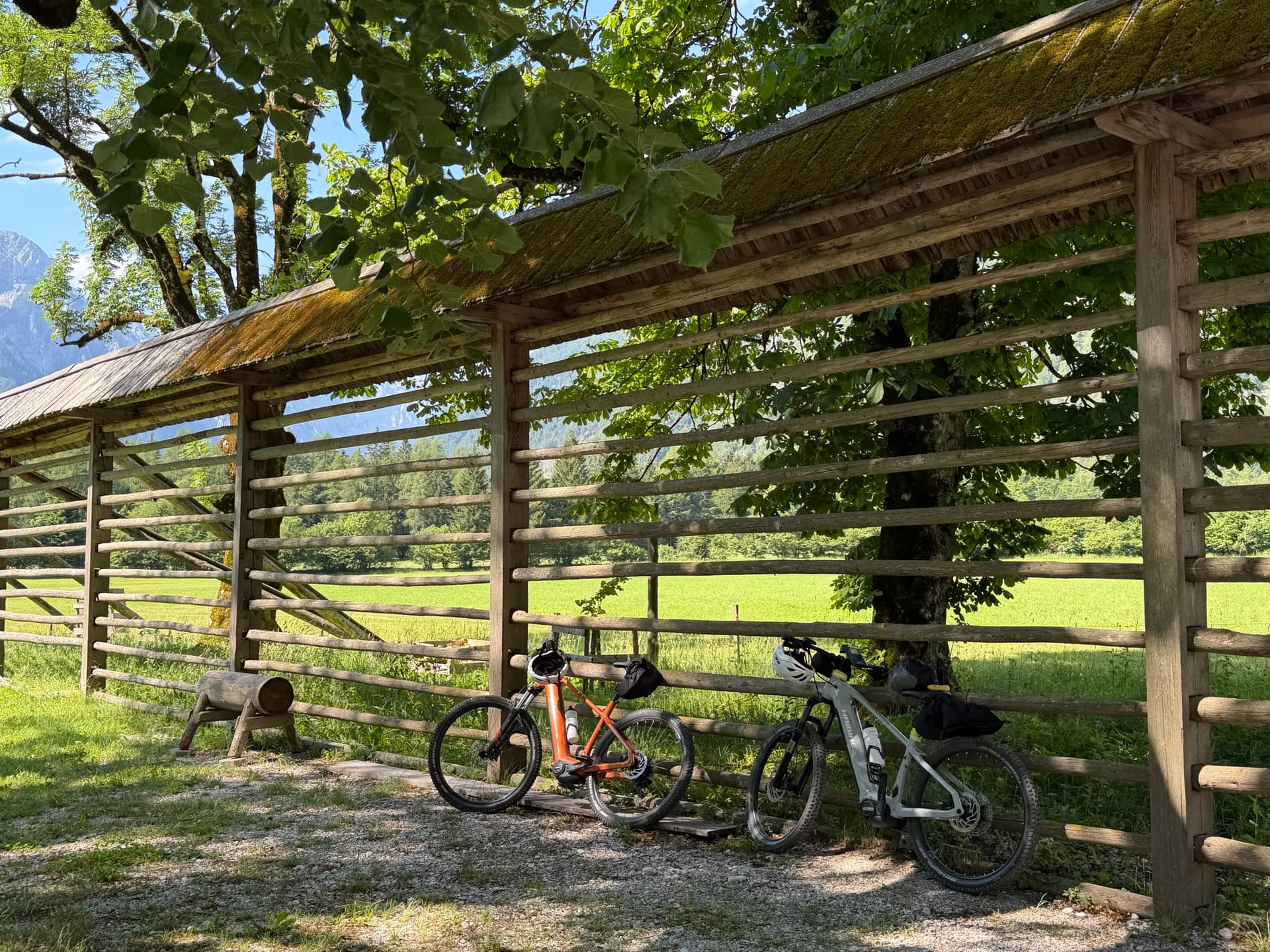 Two bicycles parked under a traditional wooden hayrack in a rural landscape