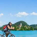 Asiatisk turist på cykel med vacker utsikt över sjön Bled med kyrka på ö i Slovenien, Europa